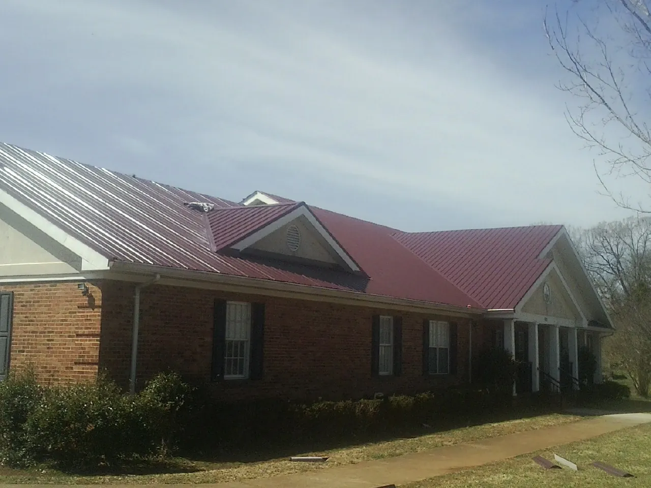 Red metal roof with gabled entries on a long brick building, from a Hail Damage Roof Repair job in Waitsburg