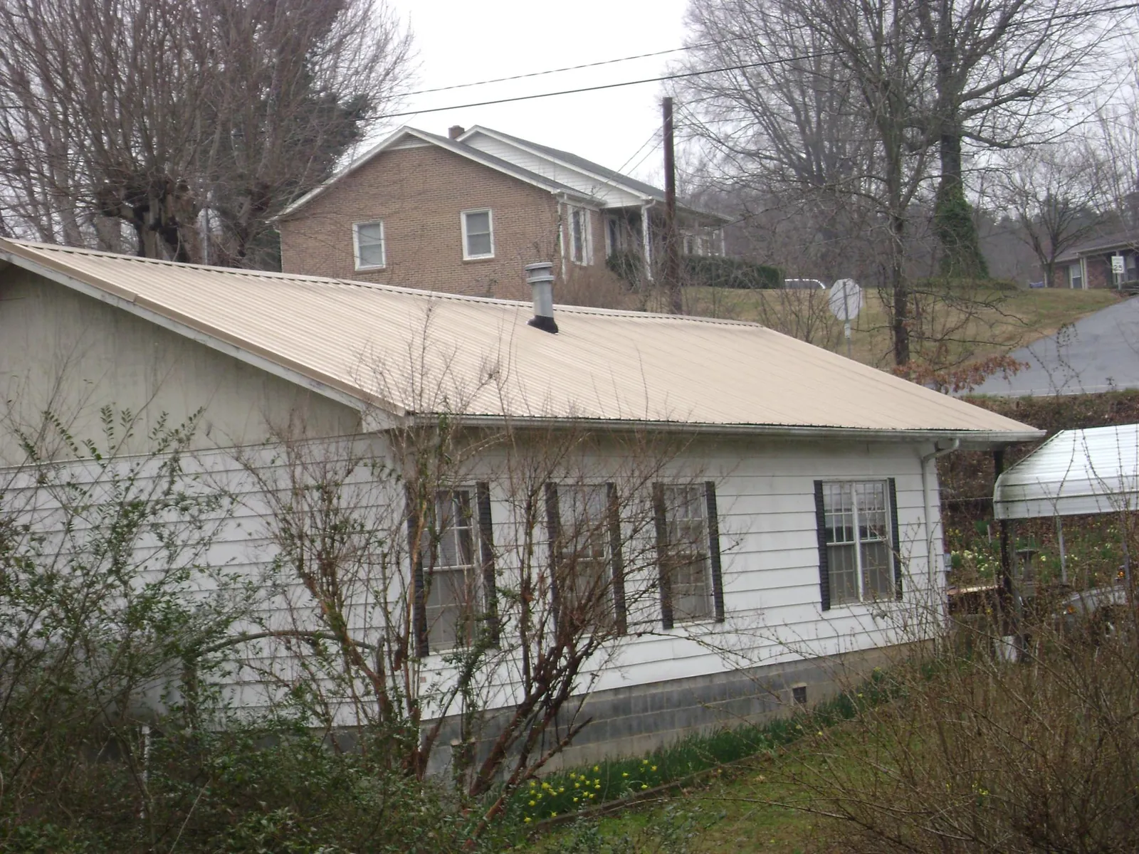 Tan metal roof on a white sided house set into a hillside — Commercial Roofing by Roofing Brothers in Waitsburg
